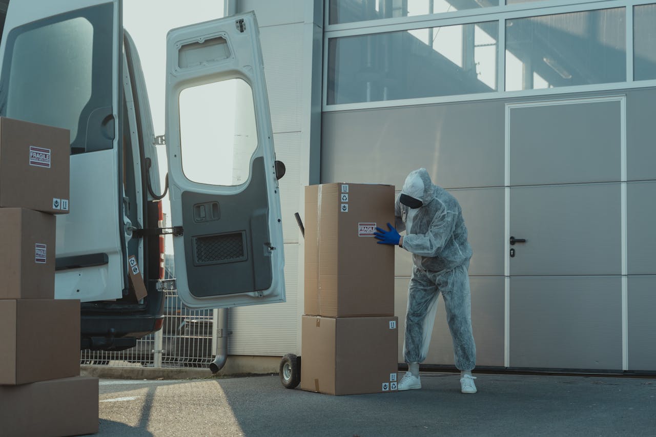 Home A delivery worker in PPE handling cardboard boxes outside a warehouse with a van.